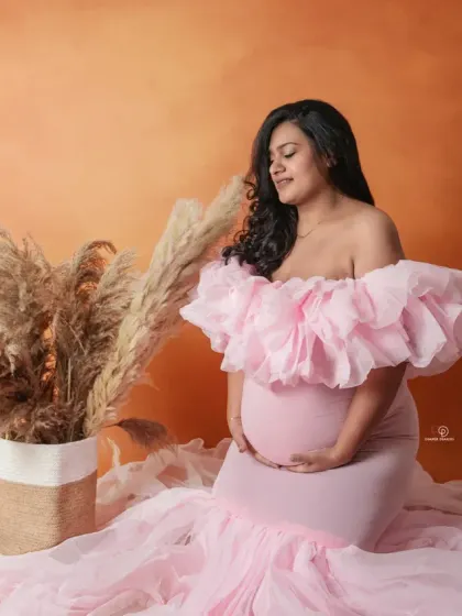 A beautiful profile of an expecting mother in a soft pink gown. The warm tones of the backdrop complement the dress perfectly, creating a gentle and loving maternity portrait.
