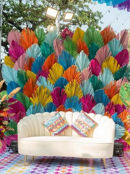 A quirky and colorful photo booth with a backdrop of paper palm leaves in rainbow hues, perfect for a fun-filled Haldi or Mehendi party.