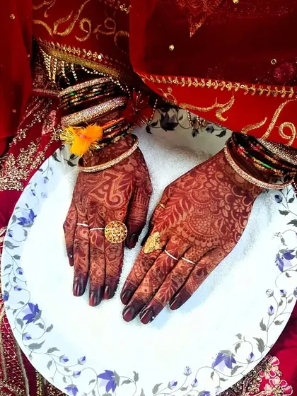 A closer look at the bride's hands during her Nikkah ceremony, showing the beautiful contrast of the dark mehendi and gold rings.