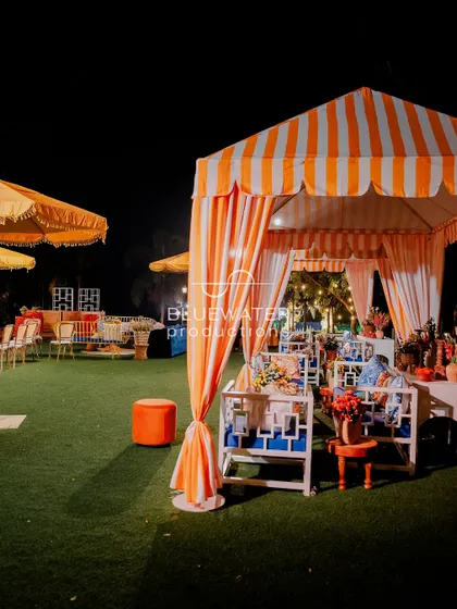 A cozy cabana with orange and white stripes provides a comfortable and stylish seating nook for guests at this outdoor Haldi function.