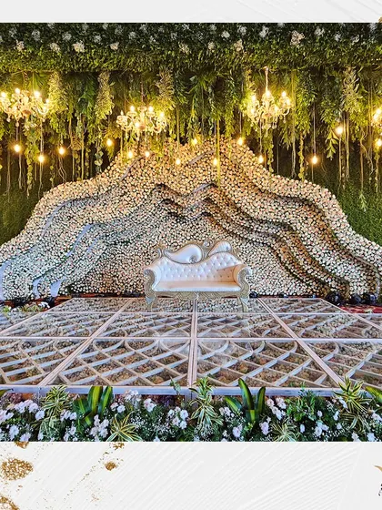 This stage design creates a sense of being nestled in a mountain of flowers. The flowing arrangement of white blooms, combined with hanging greenery and warm lights, offers a unique and organic feel.