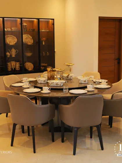 An elegant round dining table set for eight, perfect for family gatherings. The glass-fronted crockery cabinet with internal lighting beautifully displays the dinnerware, adding a touch of luxury to the dining space.