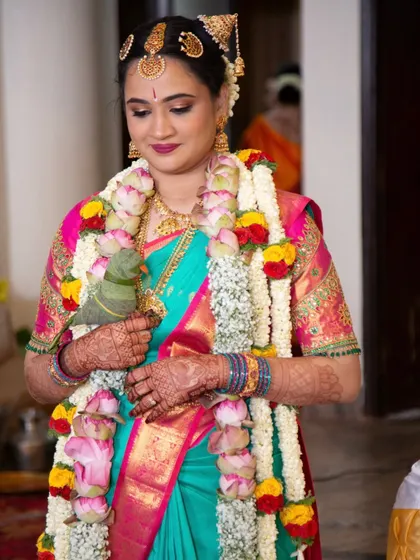 Bride Vibha, all set for her Brahmin wedding Muhurtham. She's holding the traditional parrot, and her makeup is a blend of vibrant color on the lips with soft, defined eyes.