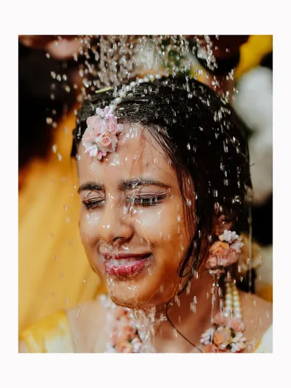 A close-up of the bride's face as she is showered with water during the Haldi ritual, a moment of refreshing joy.