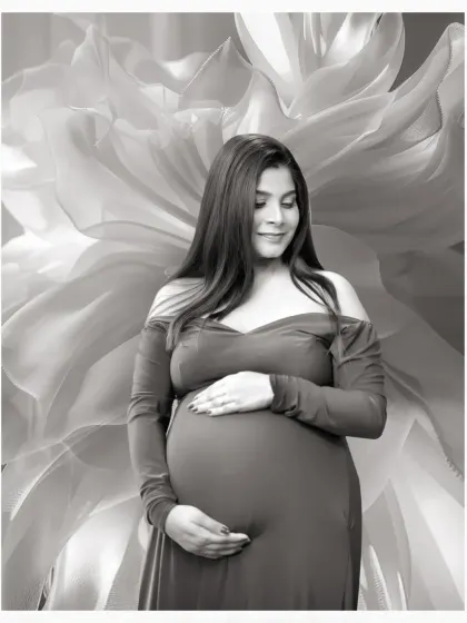 A serene black and white solo portrait of a mother-to-be cradling her bump, set against a soft, abstract floral background.