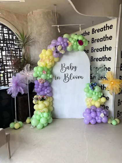 A 'Baby in Bloom' themed baby shower with a fresh pastel color palette. The decor features a personalized arched backdrop and a balloon garland in shades of lavender, yellow, and light green.