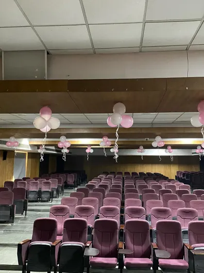 The auditorium seating area decorated with simple pink and white balloon bunches for a fresher's party.