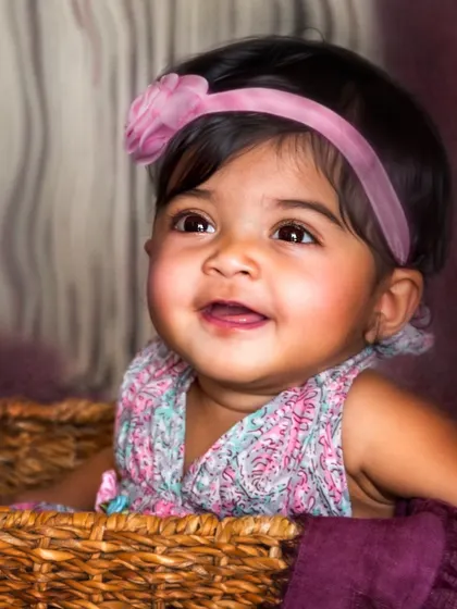 A beautiful close-up of a smiling baby girl in a basket. The warm lighting and her joyful expression create a classic, heartwarming portrait that radiates happiness.