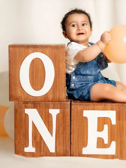 A happy baby boy celebrates turning one, sitting atop wooden blocks that spell out his big milestone. This classic studio setup is perfect for timeless first birthday portraits.