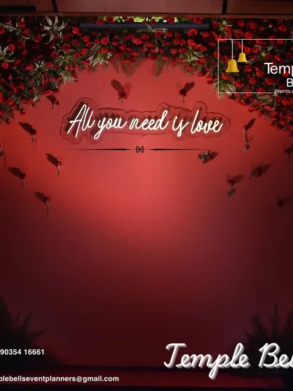 A romantic photo backdrop featuring a neon sign that reads "All you need is love". This simple yet impactful element, combined with a red floral frame, creates a perfect spot for couple and guest photos.