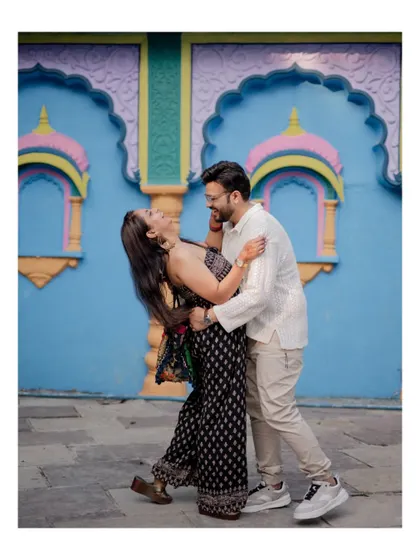 A candid shot of the couple laughing together while the groom dips his bride, set against a vibrant blue and yellow wall.