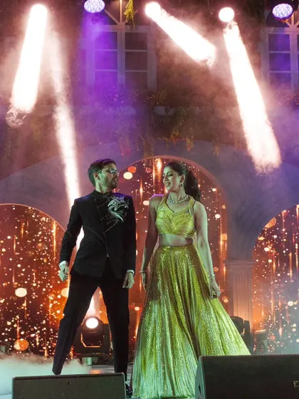 The couple commands the stage during their sangeet performance, framed by dramatic spotlights, showcasing a powerful and coordinated presence.