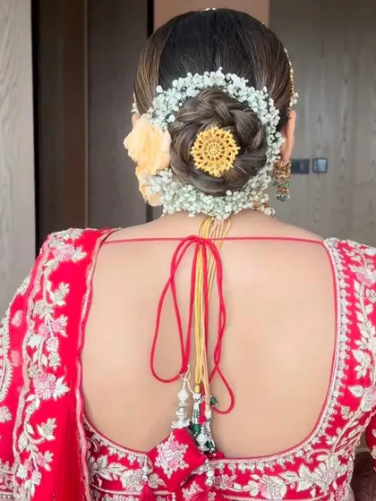 A detailed look at a bridal bun featuring a gajra of baby's breath and a central gold accessory. This combination of fresh flowers and traditional jewellery creates a rich and elegant finish.