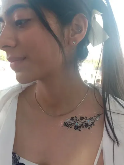 A close-up of a glittery floral branch on the collarbone. The silver glitter adds a touch of glamour to the black linework.