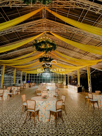A beautiful indoor dining space for a Haldi, with a ceiling of yellow drapes and floral chandeliers over tables set on a patterned floor.