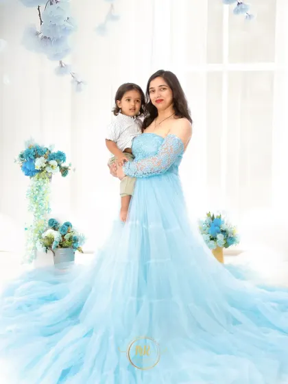A mother holds her son in a tender moment from the same blue-themed shoot. The floral props add a touch of softness and elegance to the scene.