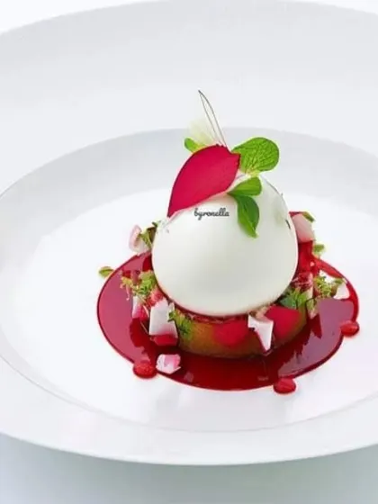 A delicate panna cotta or mousse dessert, presented with a vibrant red fruit coulis and edible flower petals. Simple, elegant, and delicious.