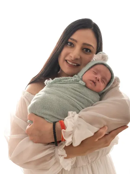 A new mother holds her swaddled baby close, smiling at the camera. The joy of new parenthood is so wonderful to capture.