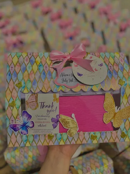 Holding up one of the butterfly-themed birthday hampers to show its lovely design and personalized tags.