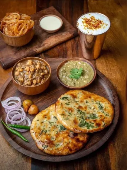 A hearty and satisfying meal of street style Chole Kulche. The spicy chickpea curry is served with soft, fluffy kulchas, pickled onions, and a glass of saffron lassi.
