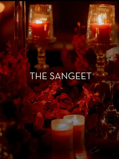A title card for 'The Sangeet', set against a close-up of the candle-lit, floral decor, setting the tone for a night of celebration.