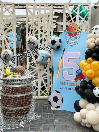 A themed cake and display area for the sports party, using a rustic barrel as a table and decorated with sports-themed balloons and props.
