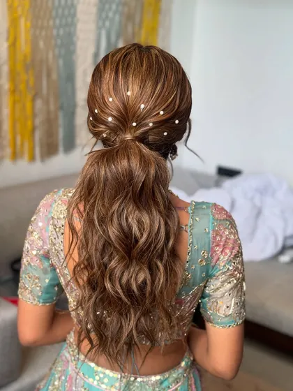 A modern and chic wavy ponytail, adorned with delicate pearls scattered throughout. This is a stunning choice for a Sangeet or reception.