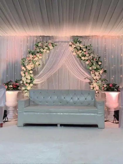 An all-white theme brings a timeless elegance to any event. This reception stage features a beautiful floral arch, soft drapery, and decorative white trees, all illuminated to create a dreamy and sophisticated setting.