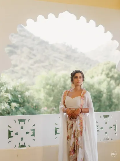 The bride standing against an arched window with the hills of Udaipur in the background. A beautiful blend of architecture and nature.