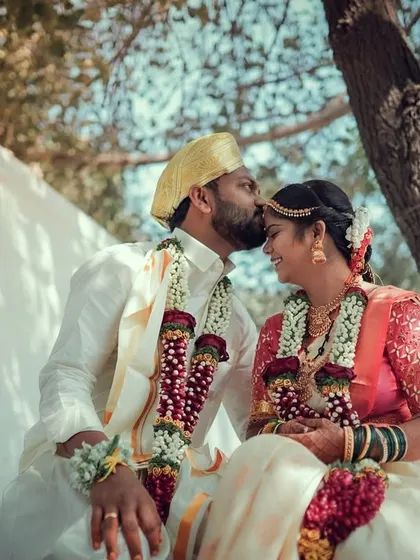 A tender forehead kiss between a newly married couple in their traditional South Indian wedding attire.