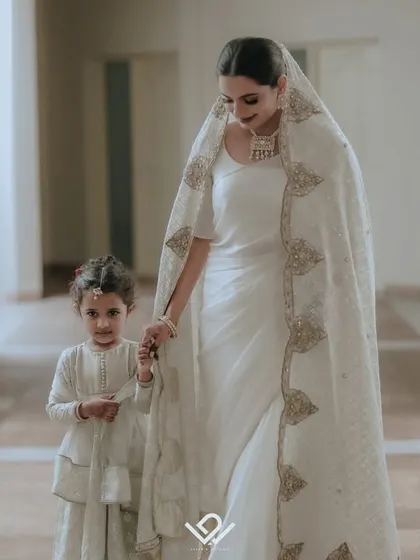 A touching moment between a Muslim bride and a young flower girl, both dressed in beautiful matching white outfits.