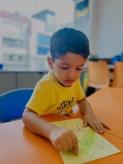 A boy points to his drawing, perhaps explaining his creation. Our classes encourage children to talk about their work, building their narrative skills.