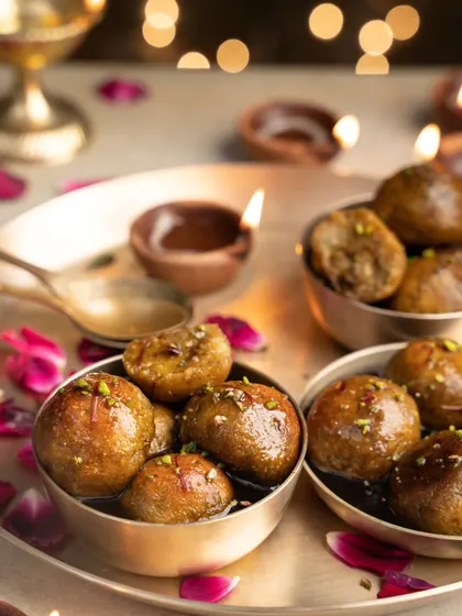 Gulab Jamun made with jaggery, glowing in the warm light of diyas. This image is all about festive indulgence, capturing the syrupy, rich quality of this beloved Indian sweet.