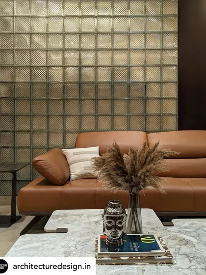 A tan leather sofa is positioned against a textured glass block wall, creating a sophisticated interplay of materials in the family lounge. The space is accessorized with natural elements for a relaxed feel.