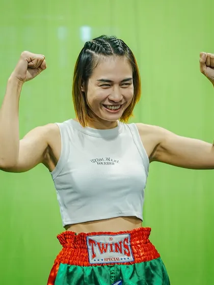 A female fighter from Thailand flexing, excited for her upcoming bout in India.