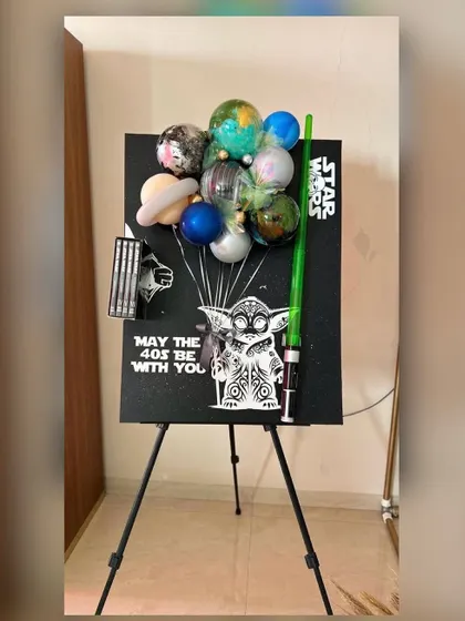 "May the 40s be with you." This creative Star Wars themed display for a 40th birthday features a custom easel with Yoda artwork, a lightsaber, and a unique balloon arrangement that looks like planets from a galaxy far, far away.
