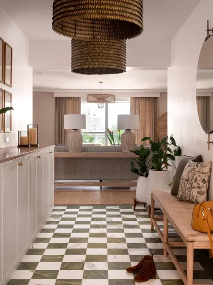 The entryway sets a relaxed yet elegant tone with its green checkered floors, woven bench, and oversized rattan pendant lights. This space immediately draws you into the home's calm, coastal-inspired world.