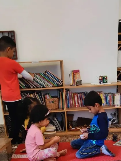 An older child spontaneously organizes a circle time for his younger friends, preparing to share a book and play a game. This is child-led community building, a natural outcome of our mixed-age environment.