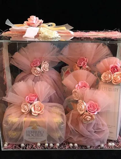 For a truly luxurious feel, we use acrylic boxes to showcase the gifts inside. Here, each item, including a box of Ferrero Rocher, is individually wrapped in pink tulle and decorated with paper flowers.