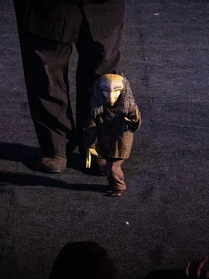 A mysterious, masked marionette character from 'Il Fil'armonico' walks towards the audience, creating a moment of intrigue.