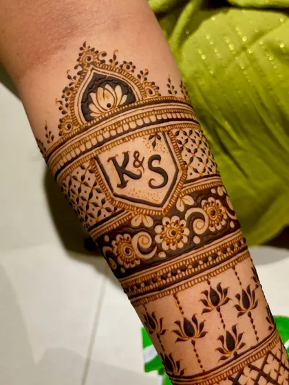 A close-up of the "K&S" initial on the forearm. The lettering is done in a stylish font, surrounded by delicate floral and geometric patterns.