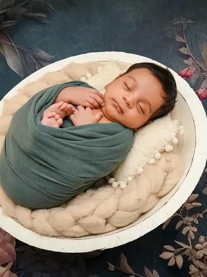 A striking portrait using a dark, moody floral backdrop. The contrast makes the peacefully sleeping baby, swaddled in teal, the clear focus of the image.
