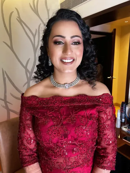 This bride's reception style is all about elegance. Her off-the-shoulder red gown is paired with beautiful curls and a radiant makeup look that highlights her smile.