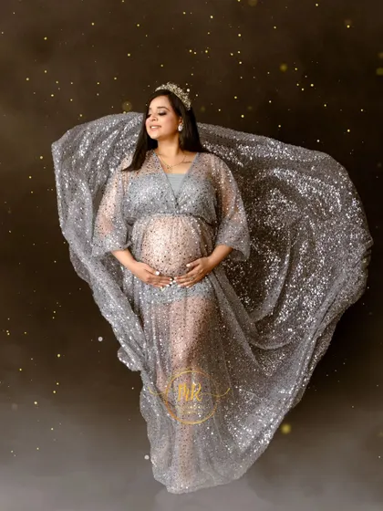 A solo portrait showcasing our sparkling silver maternity gown. The fabric is tossed to create a beautiful, flowing shape, enhanced by a magical bokeh effect.