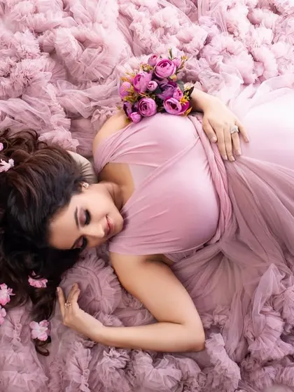 An artistic overhead shot with the client lying on a bed of soft pink ruffles. The flowers in her hair and the gentle pose create a dreamy and romantic 'sea of petals' effect.