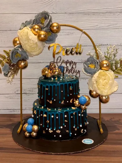 A simple, elegant, and beautiful two-tier cake. The dark teal drip on the black base, combined with the floral arch, creates a stunning and sophisticated centerpiece.