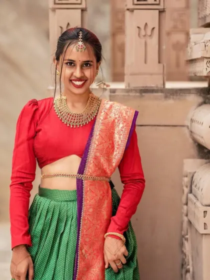 A smiling portrait of the model in the green and red Langa Dhavani, showcasing the puff-sleeve blouse design.