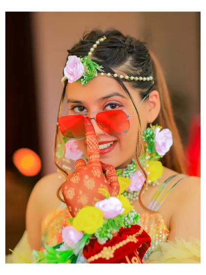 A fun and quirky bridal portrait from the Haldi ceremony. The bride's playful pose with her floral hand jewelry and sunglasses shows her personality and the joyful vibe of the event.