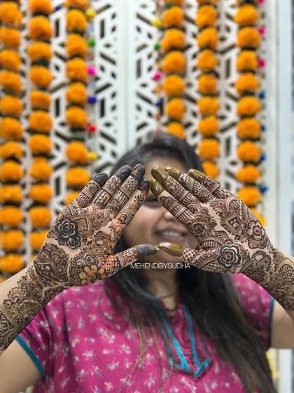 A happy client showing off her Indo-Arabic mehendi against a festive marigold backdrop.