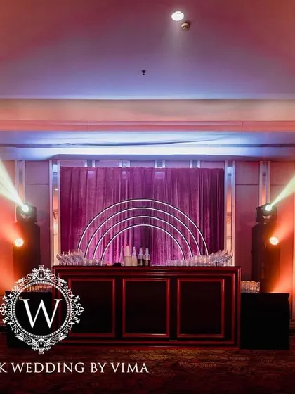 A bold and luxurious reception with a red and black color scheme. The decor includes rich red roses, modern crystal candelabras, and a stylish bar with a neon arch backdrop.